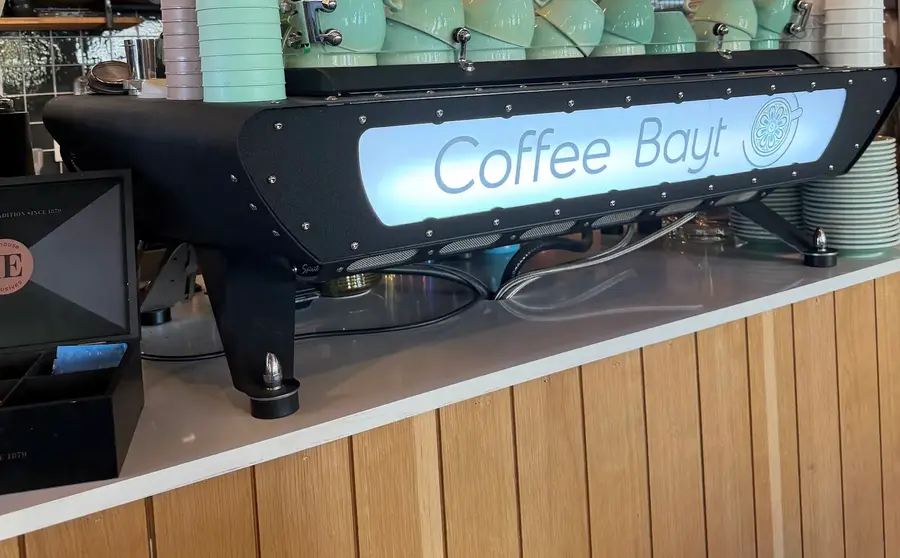 Die schwarze Siebträgermaschine mit leuchtendem Coffee-Bayt-Schriftzug und Mint-Tassen