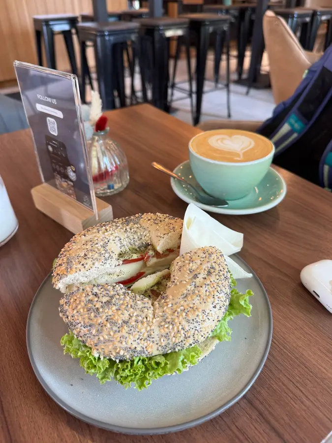 Sesam-Bagel mit Salat, daneben ein Cappuccino